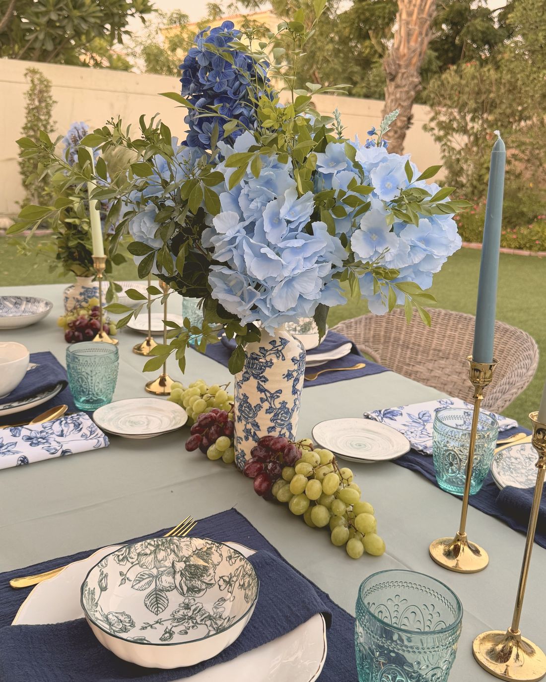 A garden table with blue hydrangeas, navy placemats and tall candles