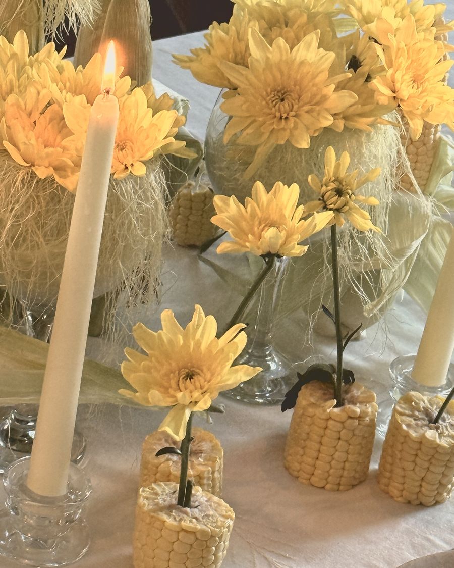 Yellow chrysanthemums tucked into corn cobs beside a lit candle