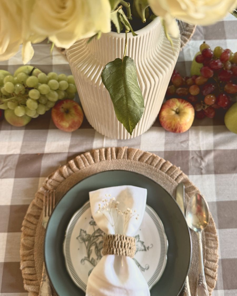 A linen napkin with a rattan ring and baby's breath beside white roses and grapes