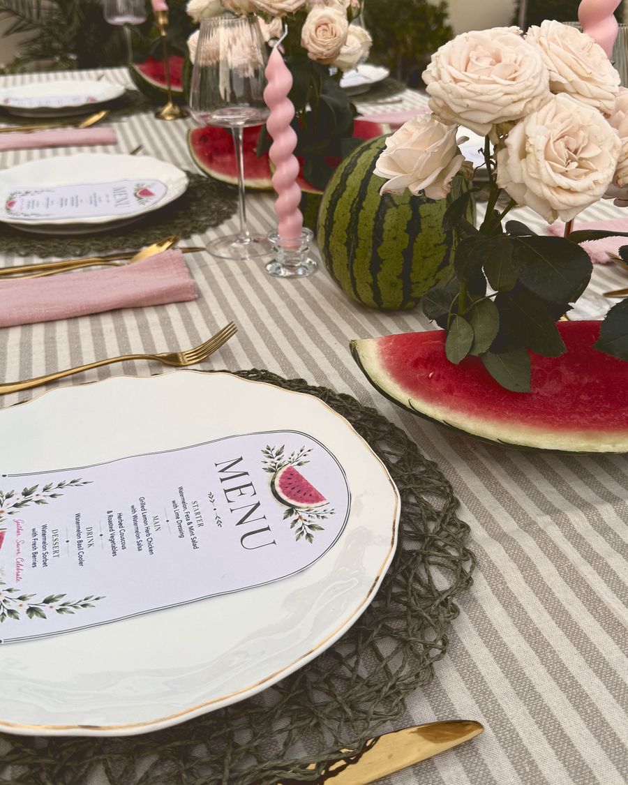 A menu card on a white plate beside pink roses and watermelon