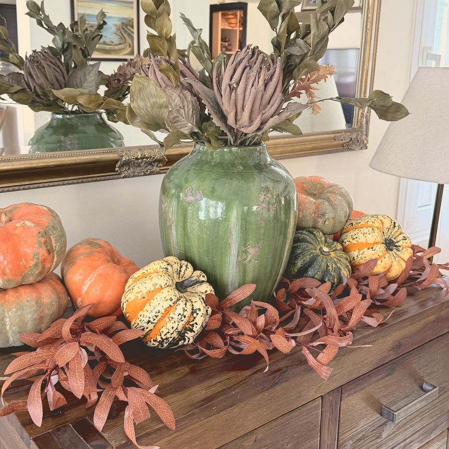 A sideboard with a green vase, pumpkins and autumn leaves