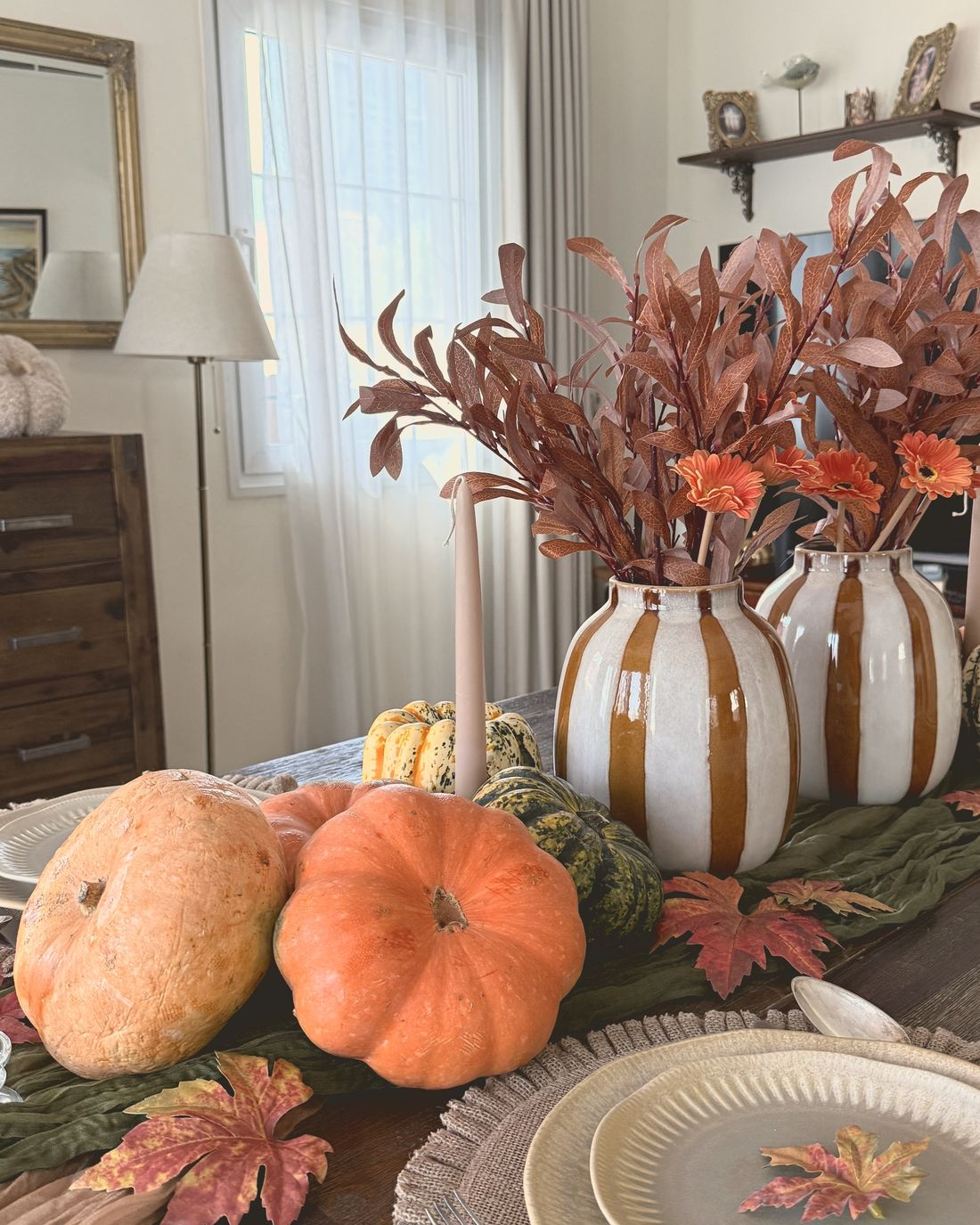 An autumn table with pumpkins, striped vases and copper leaves