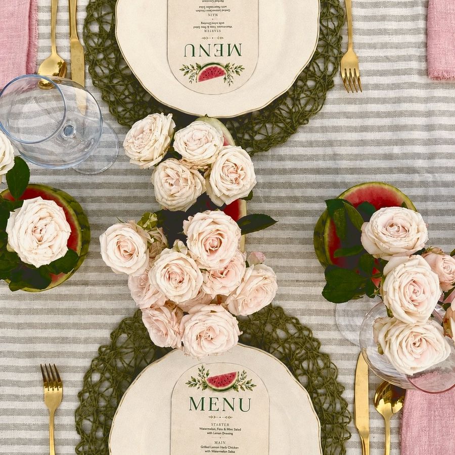 Menu cards on each plate with pink roses and watermelon between them